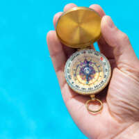 Compass in the hands of a man against the background of water. Selective focus. People.